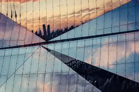 Geometryczna fasada budynku odbija niebo i sylwetki wieżowców. Efekt lustrzane odbicie photoshop.