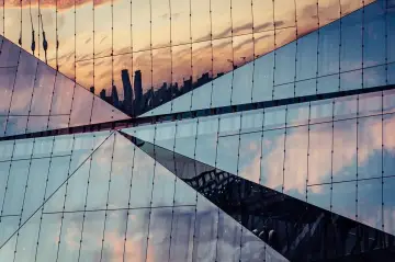 Geometryczna fasada budynku odbija niebo i sylwetki wieżowców. Efekt lustrzane odbicie photoshop.