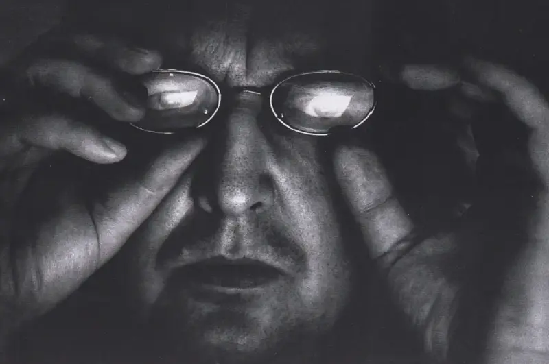 Portret Krzysztofa Gierałtowskiego w okularach, z dłońmi przy twarzy.